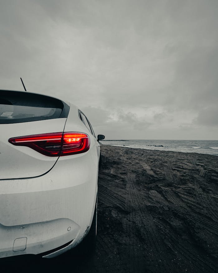 A white car parked on a sandy beach under an overcast sky, with sea waves rolling in.