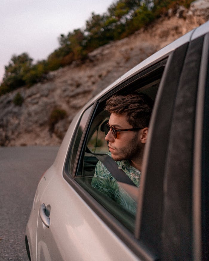 Stylish man in car gazing at scenic view through open window during a road trip.